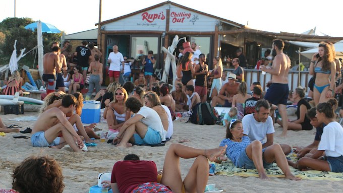 Crowd relaxing on the sand in front of Rupi's Chilling Out beach bar at Porto Pollo at sunset